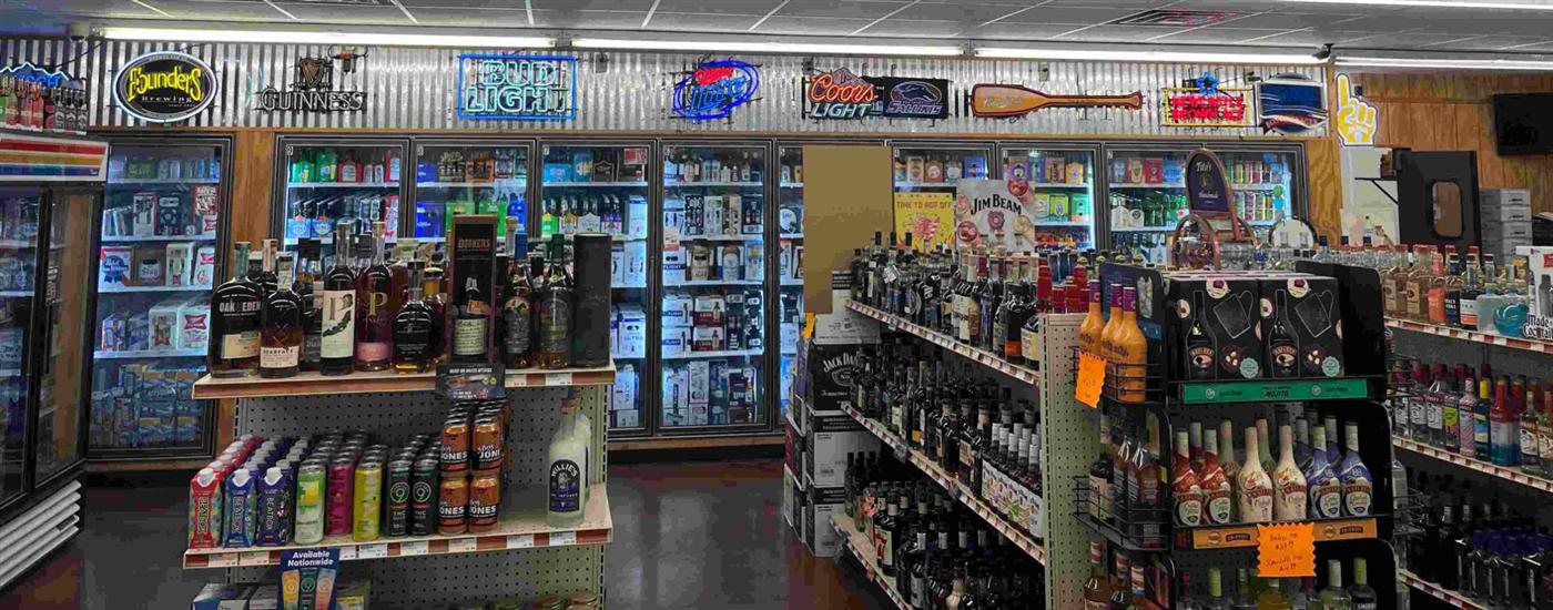 Beer cooler wall, neon brewery signs, and bourbon shelf inside AJ's Beer, Wine & Spirits